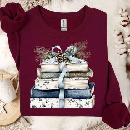 Maroon Gildan sweatshirt with a stack of blue and white books, blue ribbon, evergreen, and pinecone design.