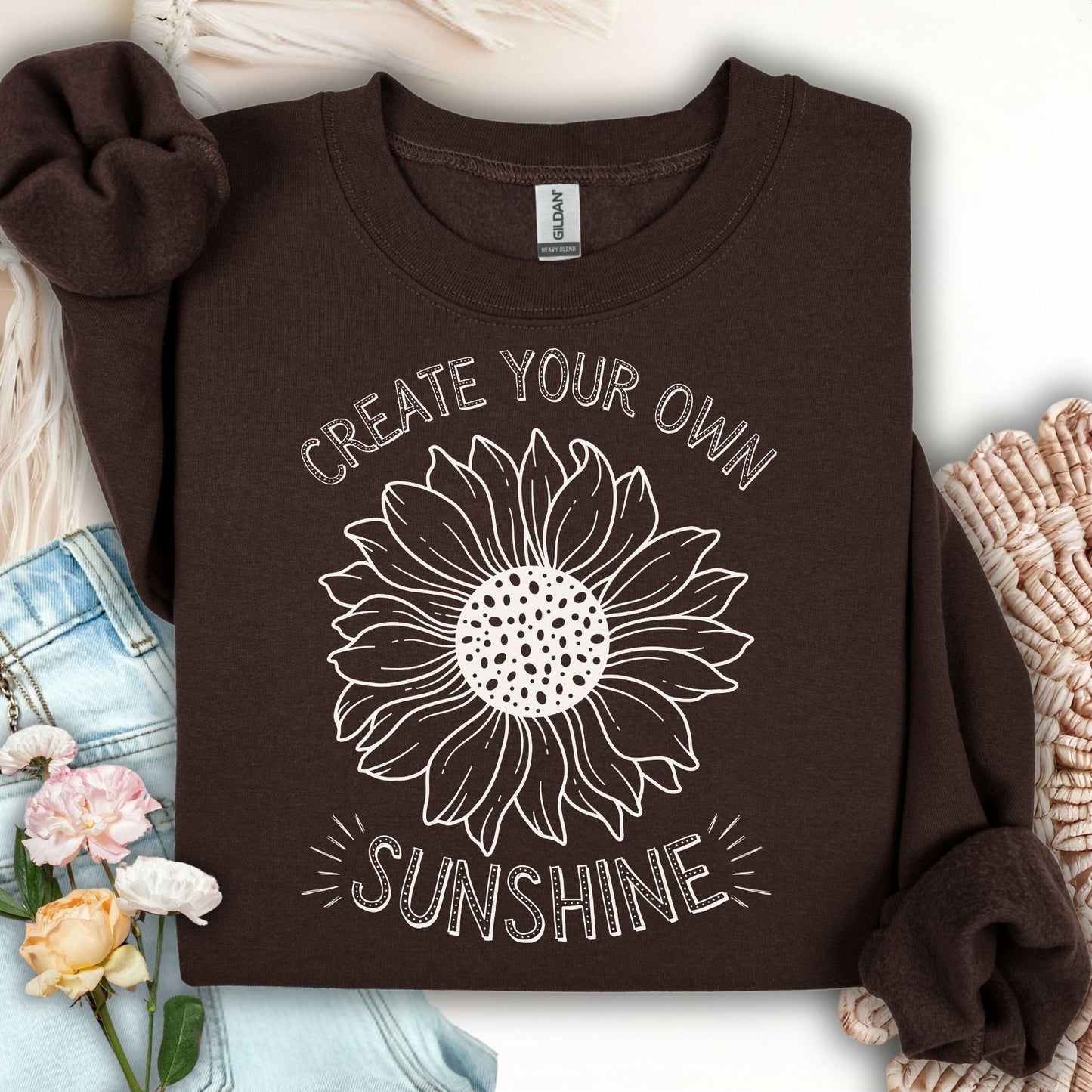 Dark chocolate unisex crewneck sweatshirt with a white hand-drawn sunflower and "Create Your Own Sunshine" text.