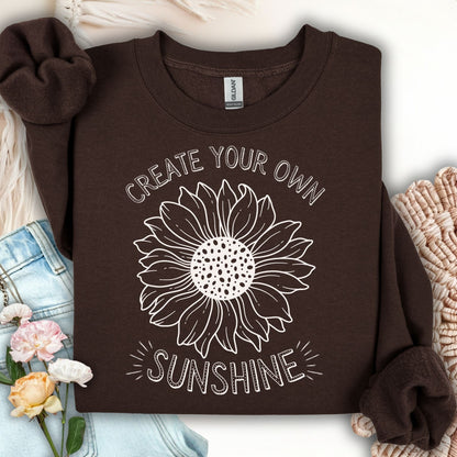 Dark chocolate unisex crewneck sweatshirt with a white hand-drawn sunflower and "Create Your Own Sunshine" text.