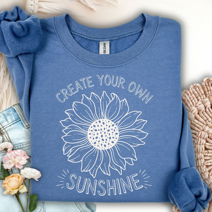 Indigo Blue S sweatshirt with "Create Your Own Sunshine" sunflower design, folded on a cozy surface.