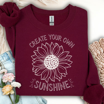 Maroon sweatshirt with "Create Your Own Sunshine" text and a hand-drawn sunflower sketch.