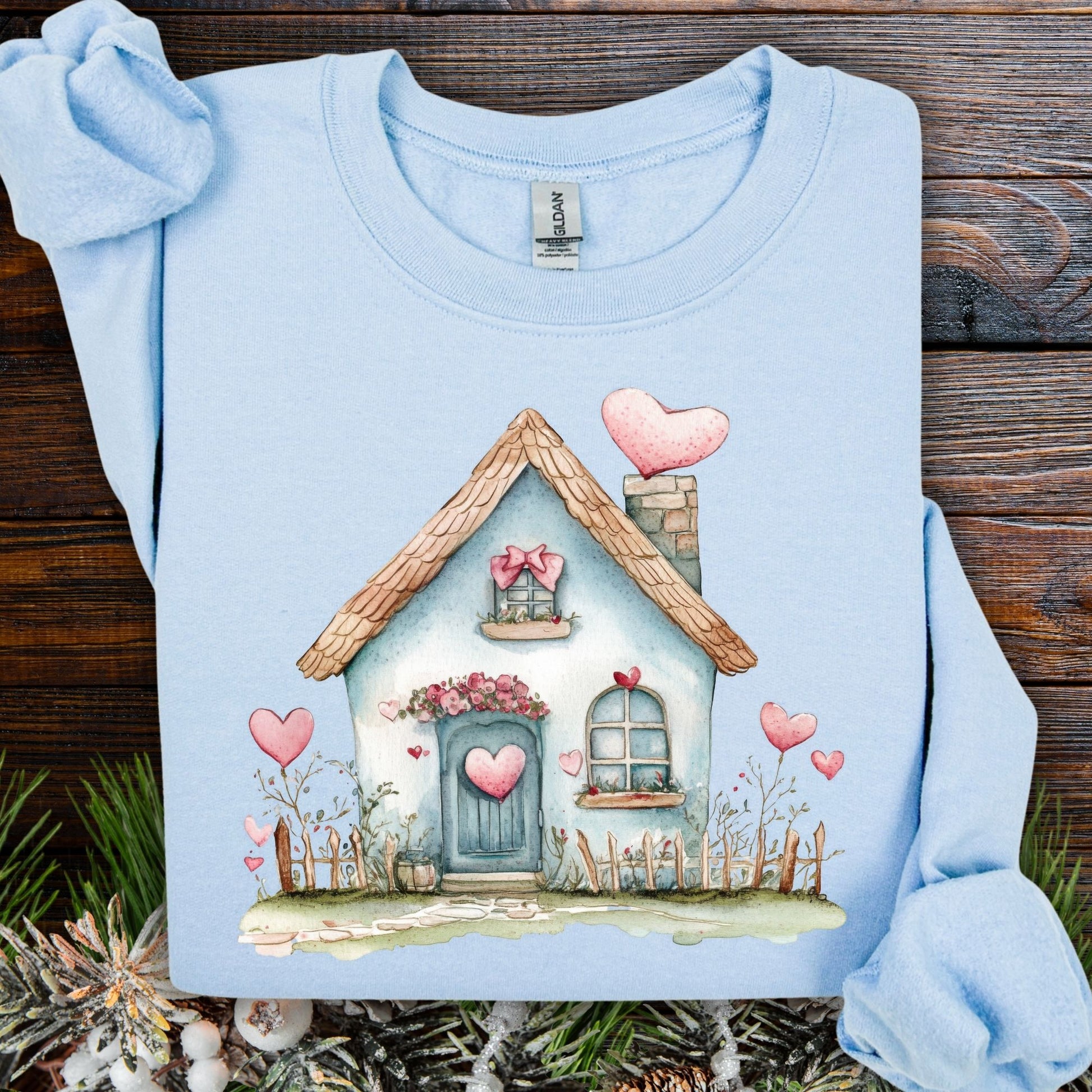 Light blue heavy blend sweatshirt with a watercolor design of a charming cottage adorned with pink hearts.