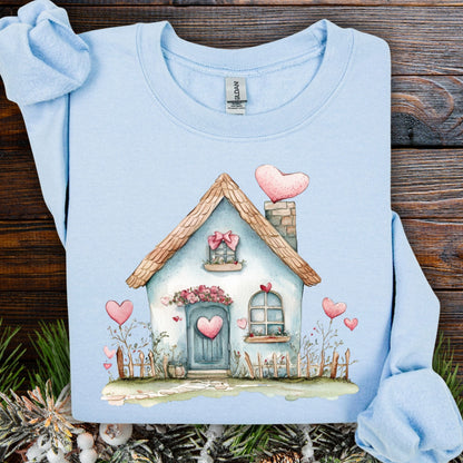 Light blue heavy blend sweatshirt with a watercolor design of a charming cottage adorned with pink hearts.