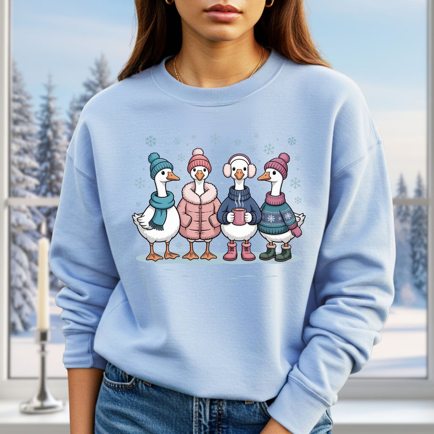 Light blue sweatshirt with four cartoon geese in winter clothes, hats, and mittens, drinking hot chocolate.
