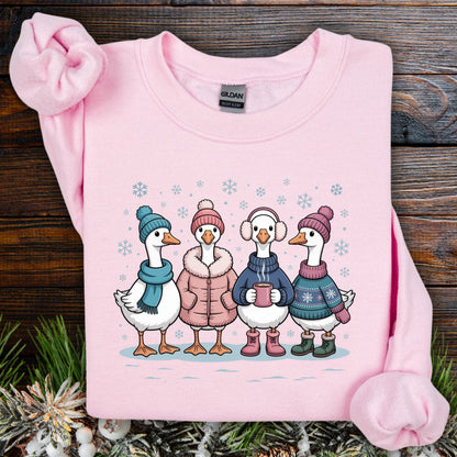 Light pink Gildan sweatshirt with four cartoon geese in winter clothes, drinking hot chocolate in snow.