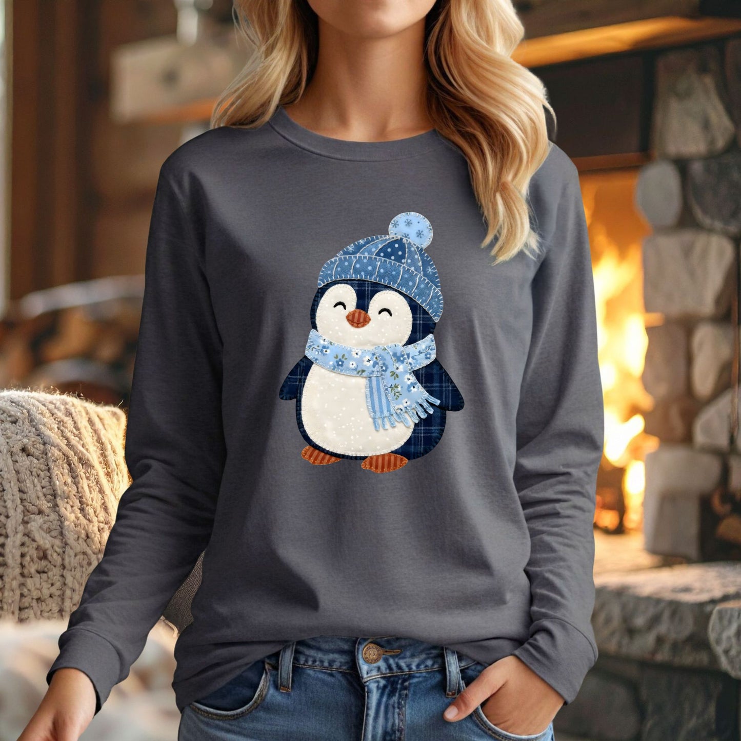 Woman in a gray long-sleeve tee with a faux patchwork winter penguin in a blue hat and scarf.