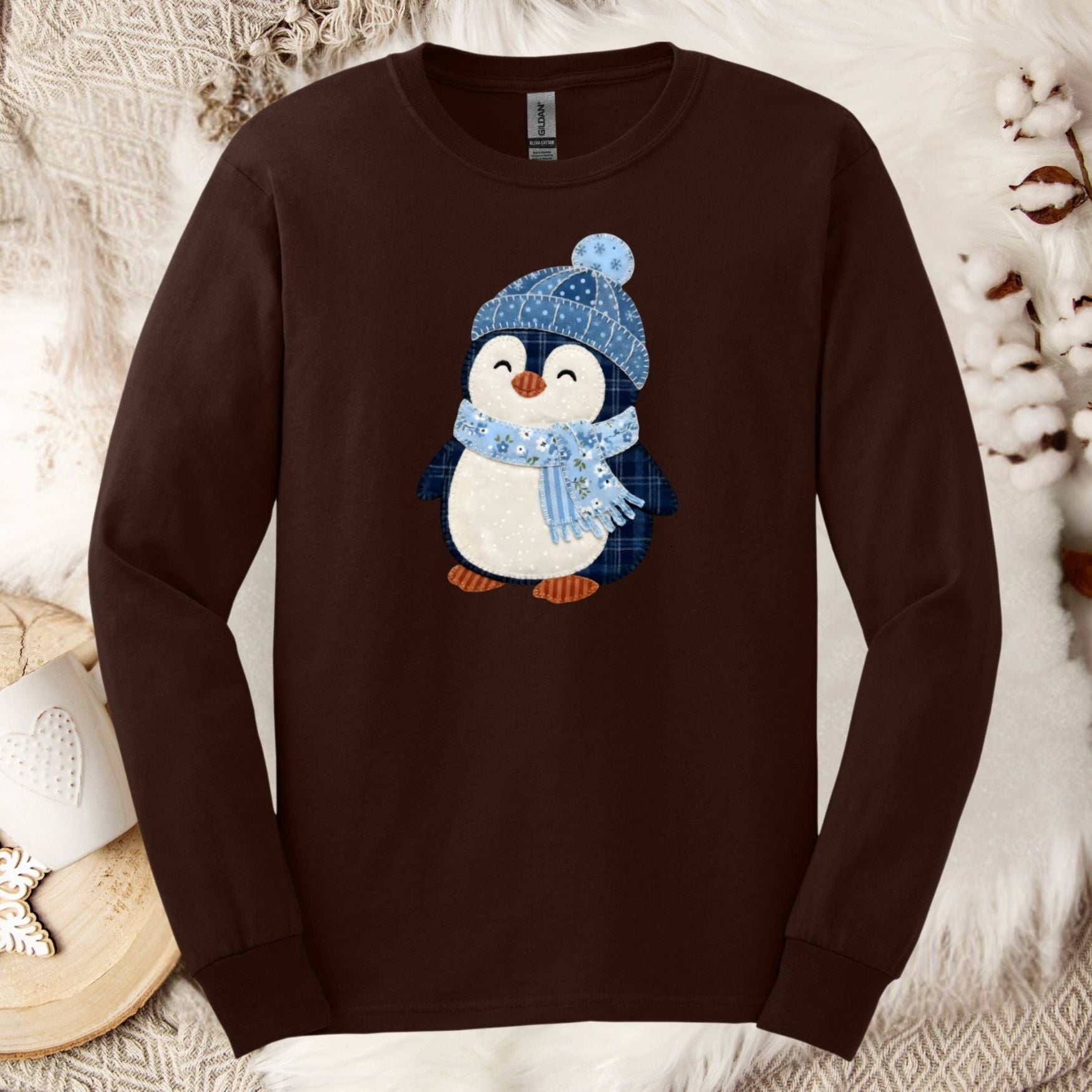 Brown long-sleeve tee with a faux patchwork winter penguin wearing a blue hat and scarf.