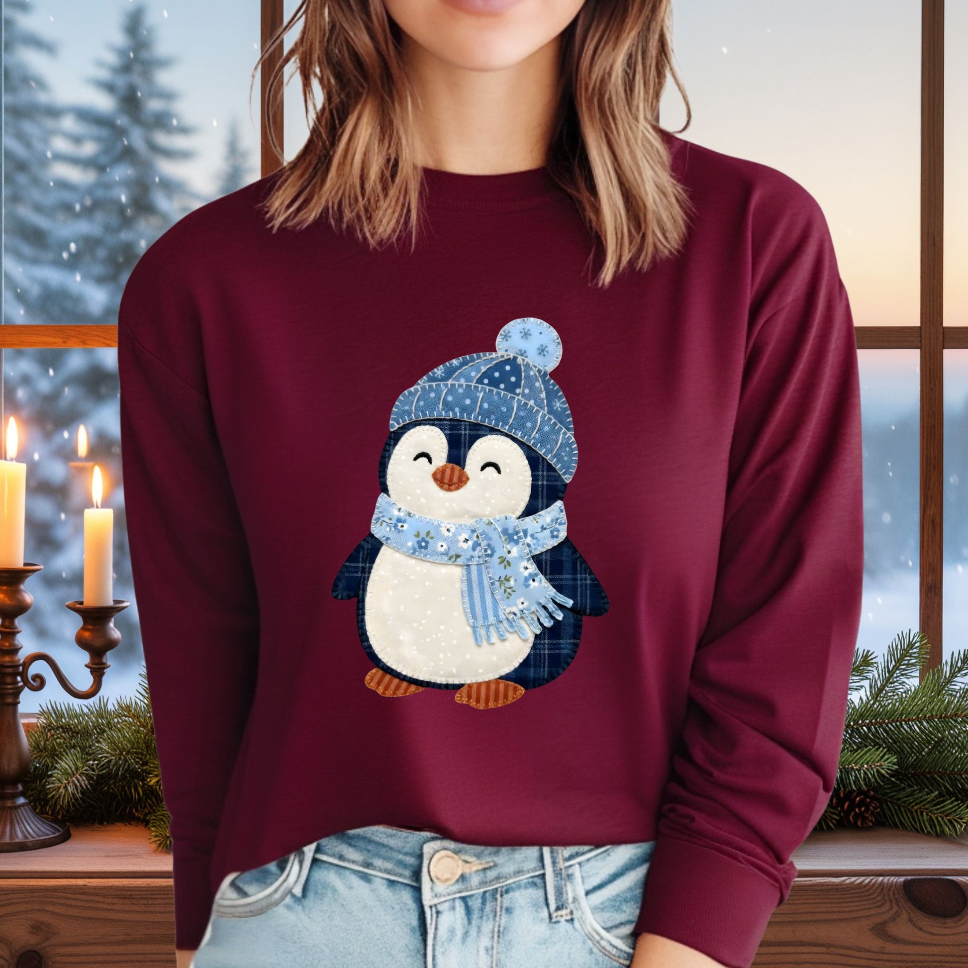 Woman wearing a burgundy long-sleeve tee with a faux patchwork winter penguin in a blue hat and scarf.