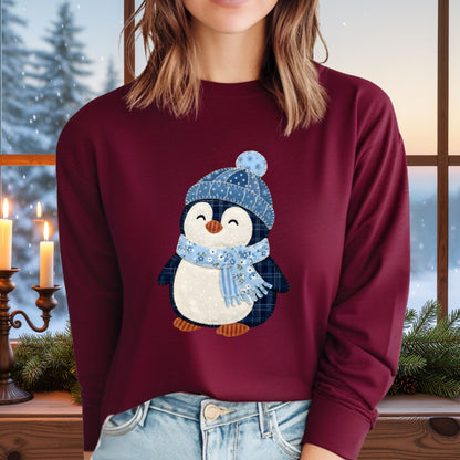 Woman wearing a burgundy long-sleeve tee with a faux patchwork winter penguin in a blue hat and scarf.