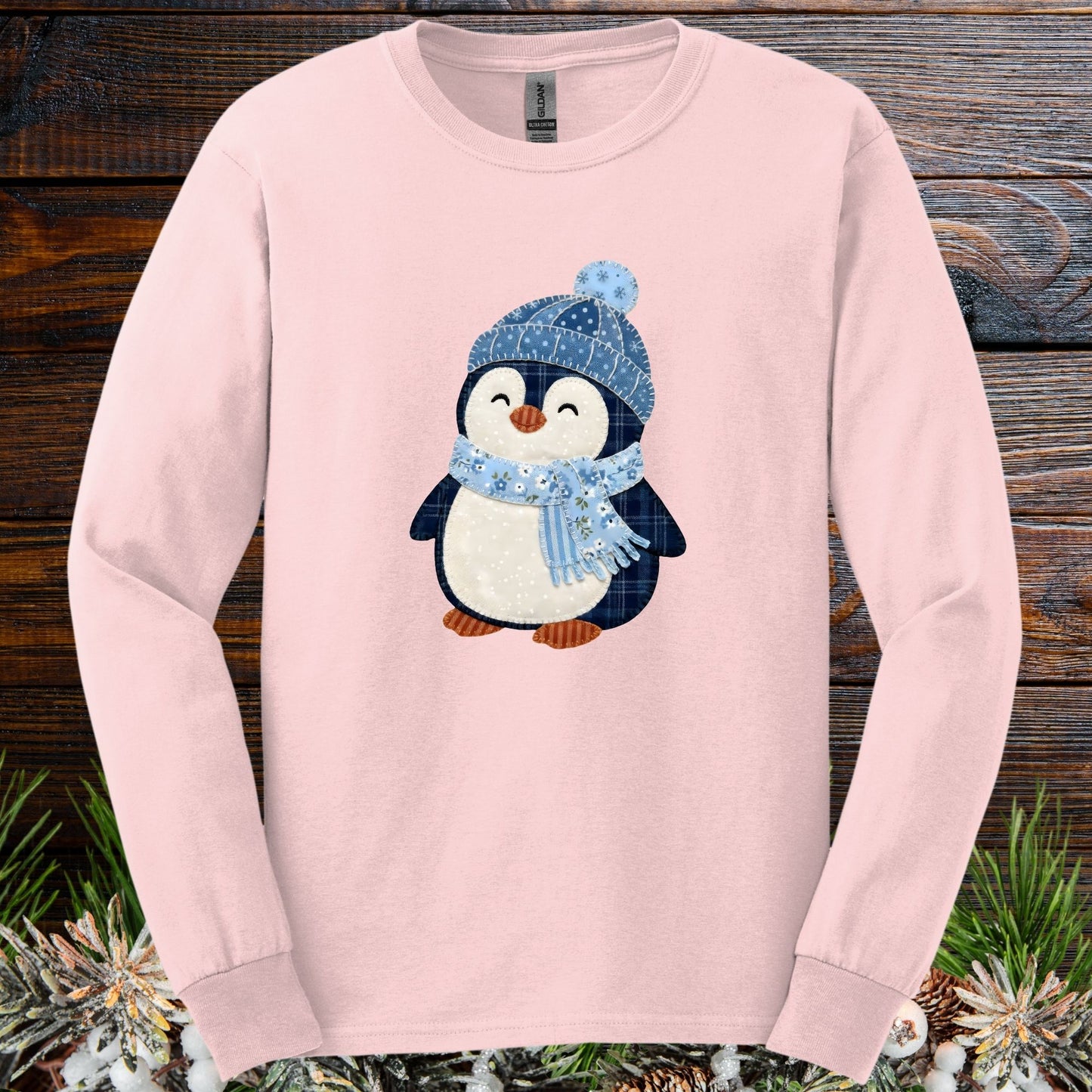 Light pink long sleeve tee with a cute faux patchwork winter penguin in a blue hat and scarf.