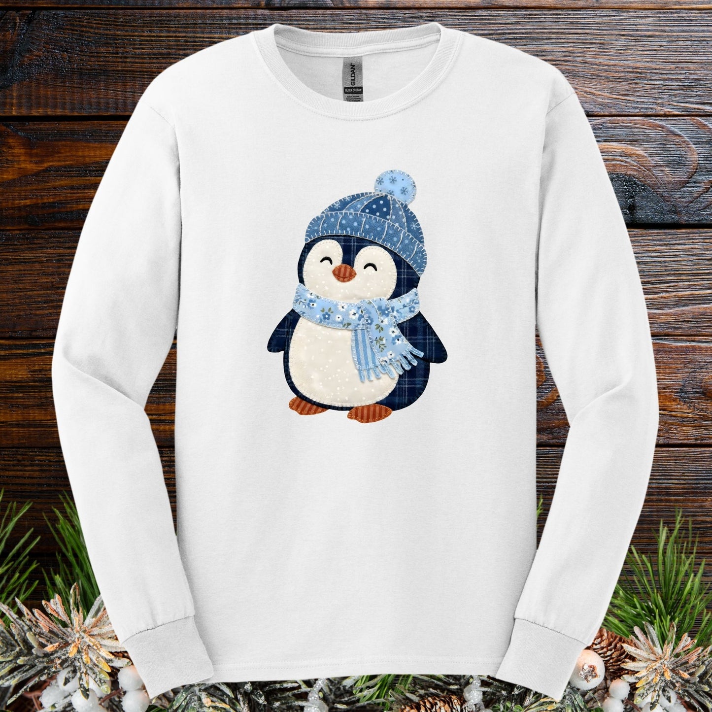 White long-sleeve tee with a cute faux patchwork winter penguin wearing a blue hat and scarf.