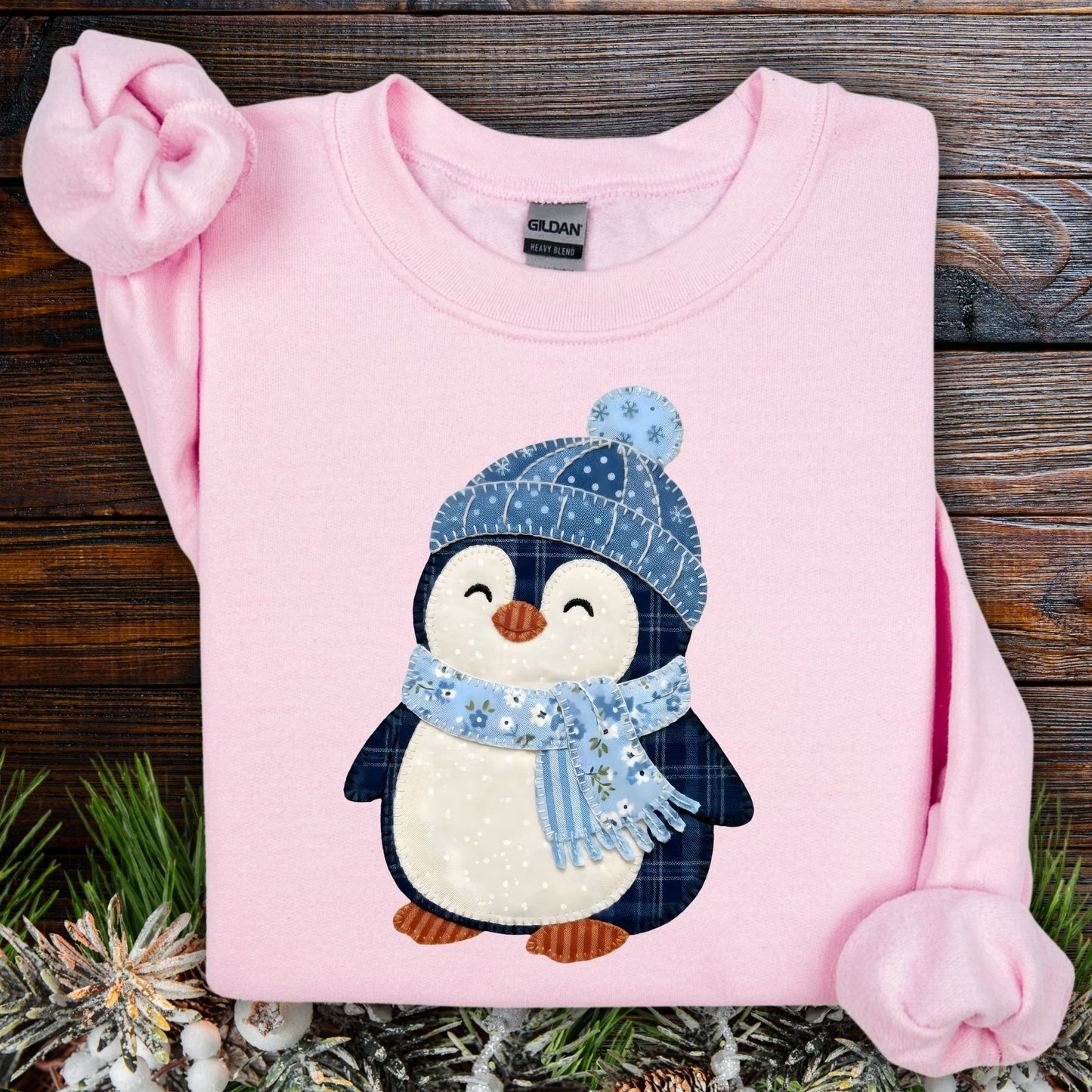 Light pink Gildan heavy blend sweatshirt with a cute faux patchwork penguin wearing a blue hat and scarf.