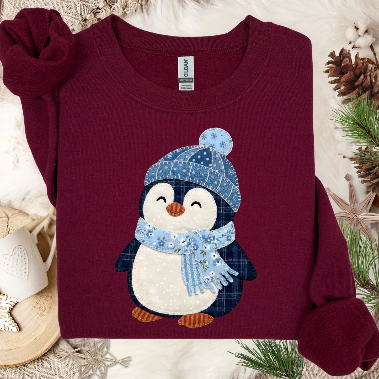 Maroon heavy blend sweatshirt with a cute faux patchwork penguin wearing a blue hat and scarf.
