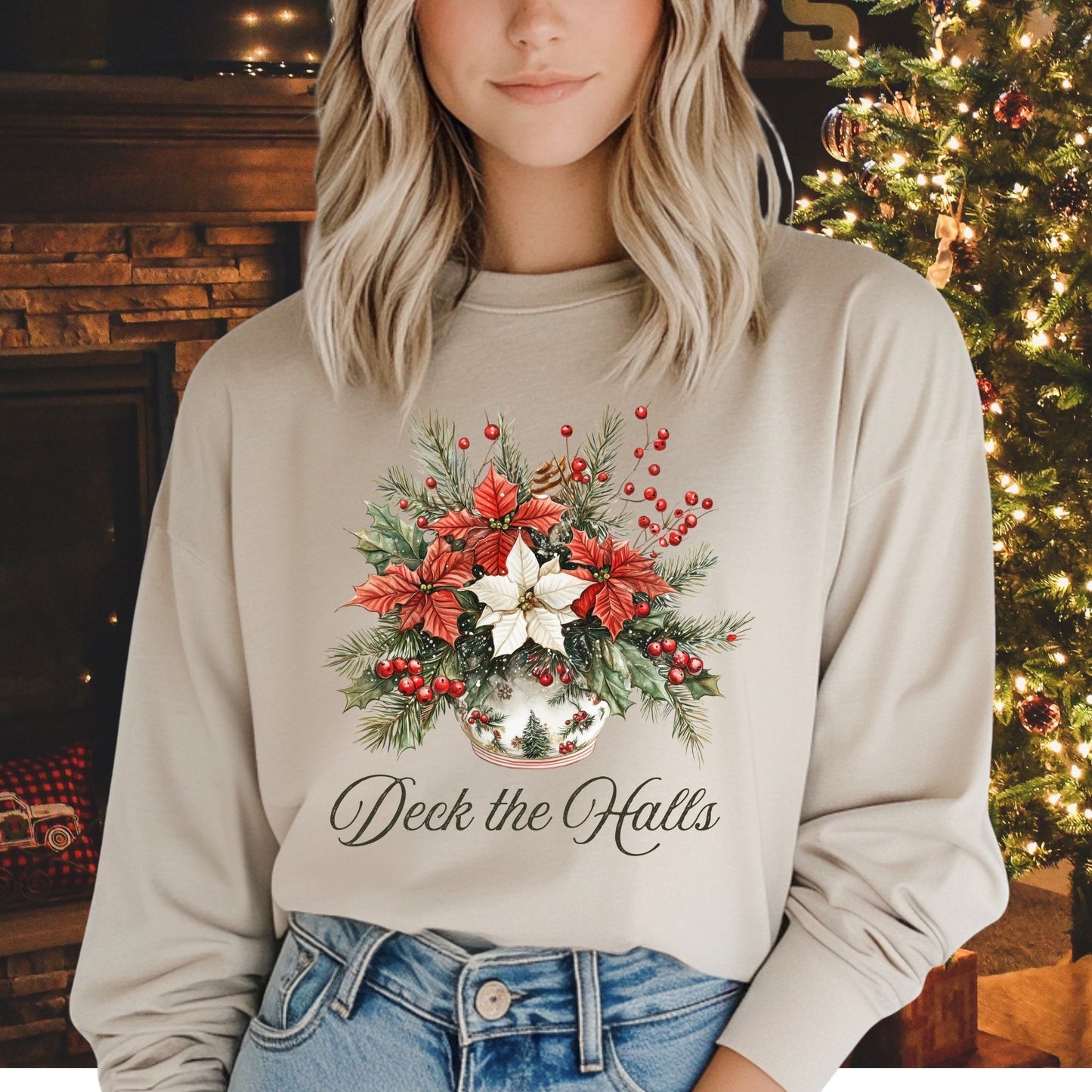 Woman in a beige long sleeve tee with a watercolor poinsettia arrangement and "Deck the Halls" script.