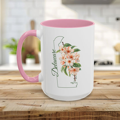 White ceramic mug with pink handle and interior, featuring a green Delaware outline and peach blossom watercolor art.