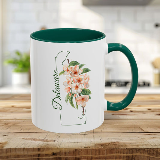 White 11oz ceramic mug with green handle and interior, featuring a Delaware outline and peach blossom art.