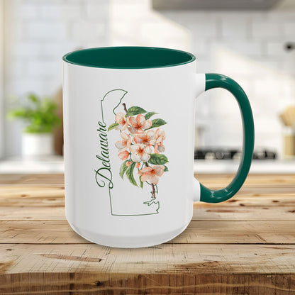15oz white ceramic mug with green handle/interior, featuring Delaware state outline and peach blossom art.