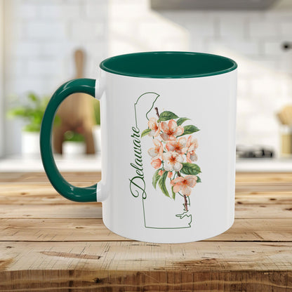 White ceramic mug with green handle and interior, featuring a watercolor Delaware state outline and peach blossoms.
