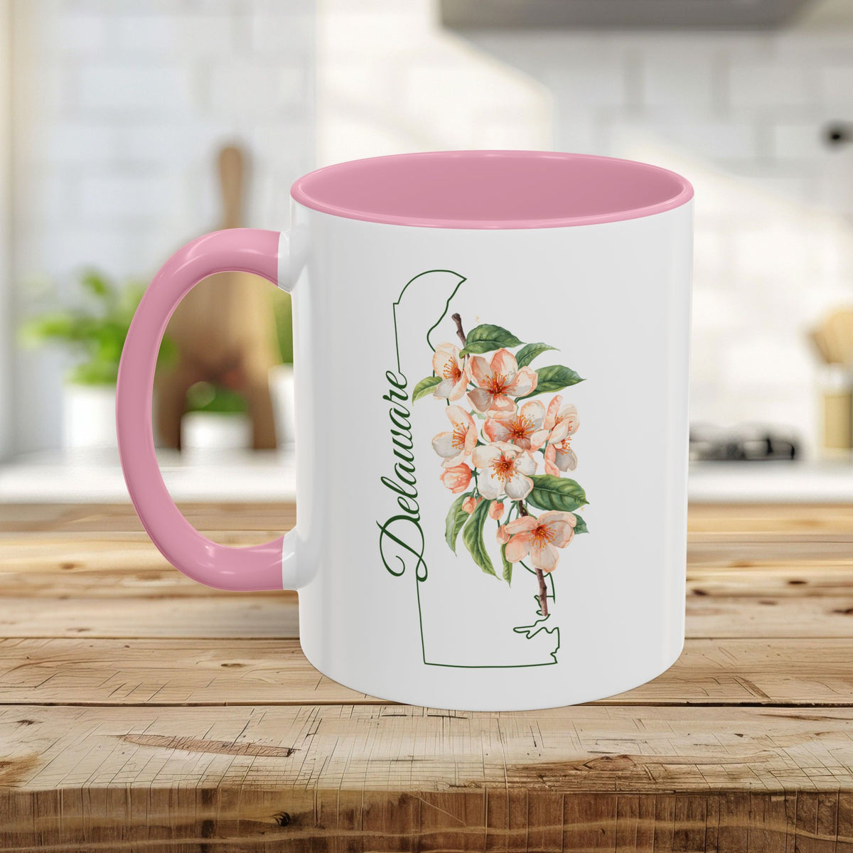 White ceramic mug with pink handle and interior, featuring a Delaware state outline and peach blossom floral design.