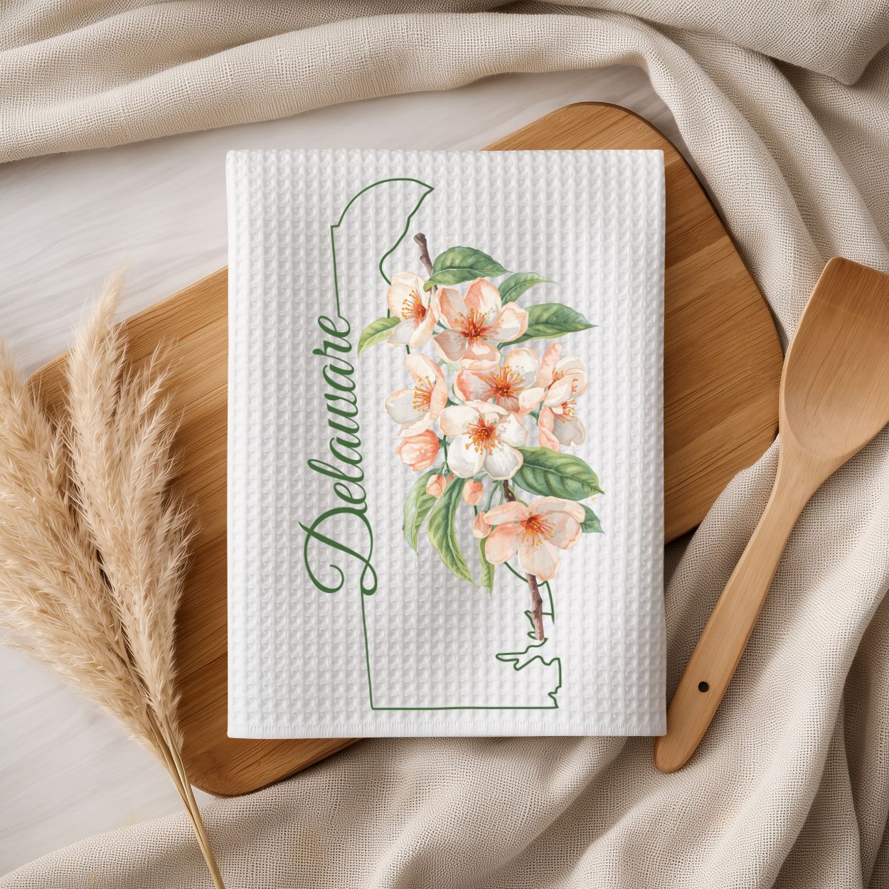 White microfiber tea towel with peach blossoms, "Delaware" script, and state outline on a wooden board.
