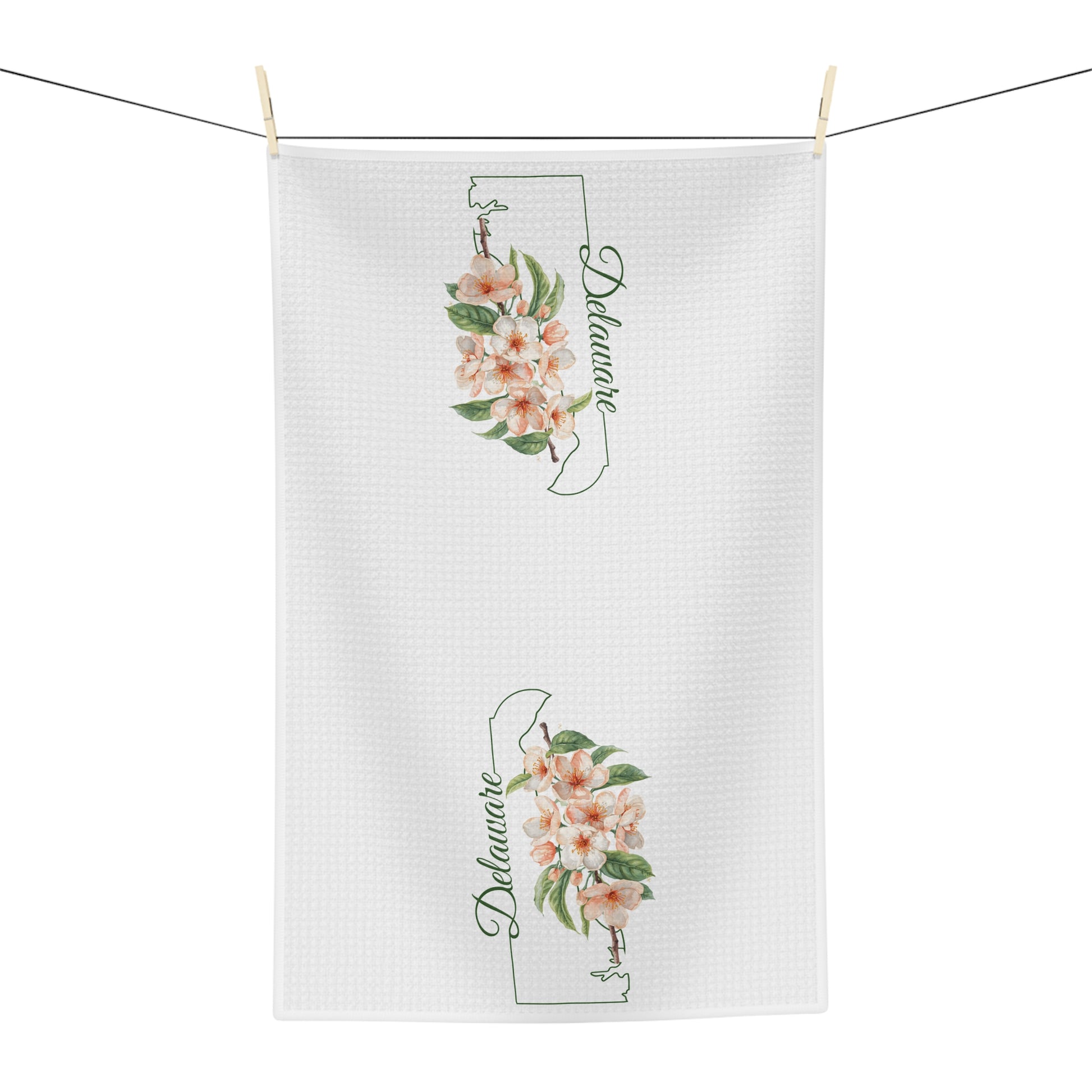 White microfiber tea towel with peach blossoms and "Delaware" script, hanging on a clothesline.