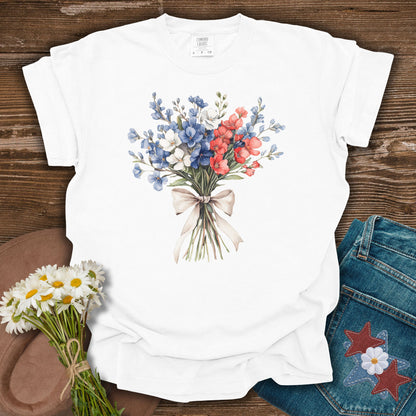 White S t-shirt with a watercolor patriotic bouquet of red, white, and blue flowers tied with a ribbon.