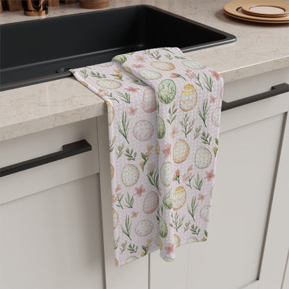 Pastel pink microfiber tea towel with watercolor Easter eggs and spring sprigs, draped over a kitchen counter.