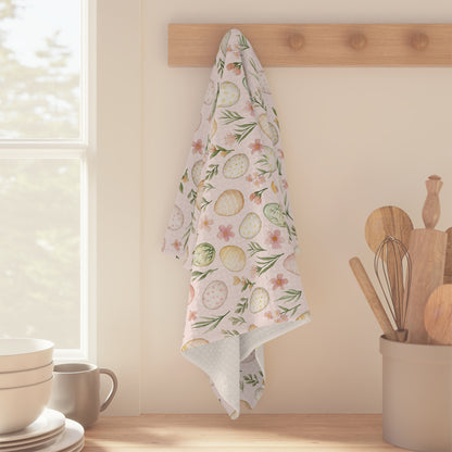 Pastel pink microfiber tea towel with watercolor Easter eggs and spring sprigs, hanging on a wooden peg.