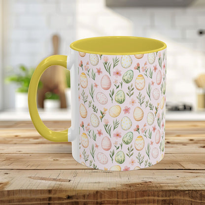 Ceramic mug with pastel watercolor Easter eggs & flowers, yellow interior/handle, on a wooden table.
