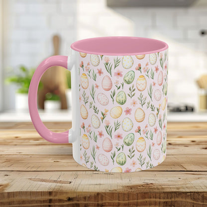 Ceramic mug with pastel watercolor Easter eggs and sprigs, pink handle and interior, on a wooden table.