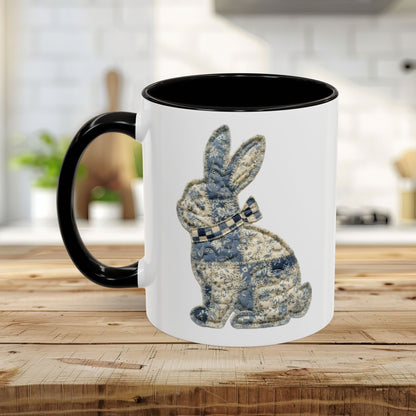 White ceramic coffee mug with black handle and interior, featuring a blue patchwork bunny illustration.