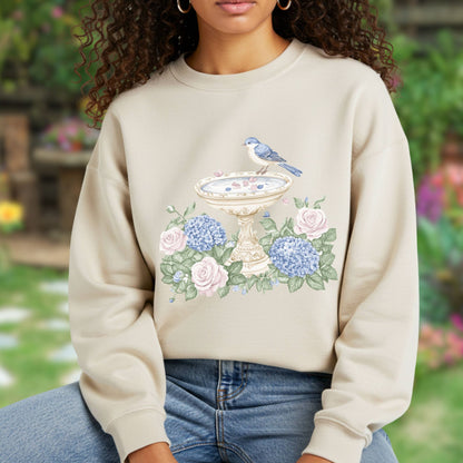 Beige sweatshirt with a watercolor bird bath, blue bird, pink roses, and blue hydrangeas design.