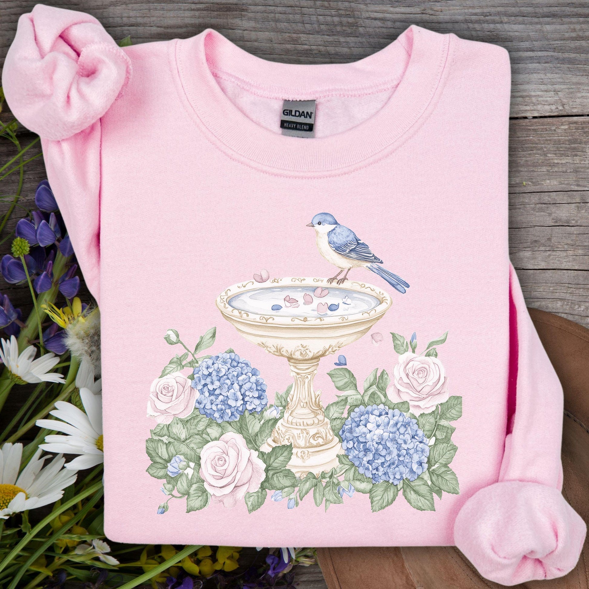 Pink Gildan sweatshirt with a watercolor bird bath, blue bird, roses, and hydrangeas design.