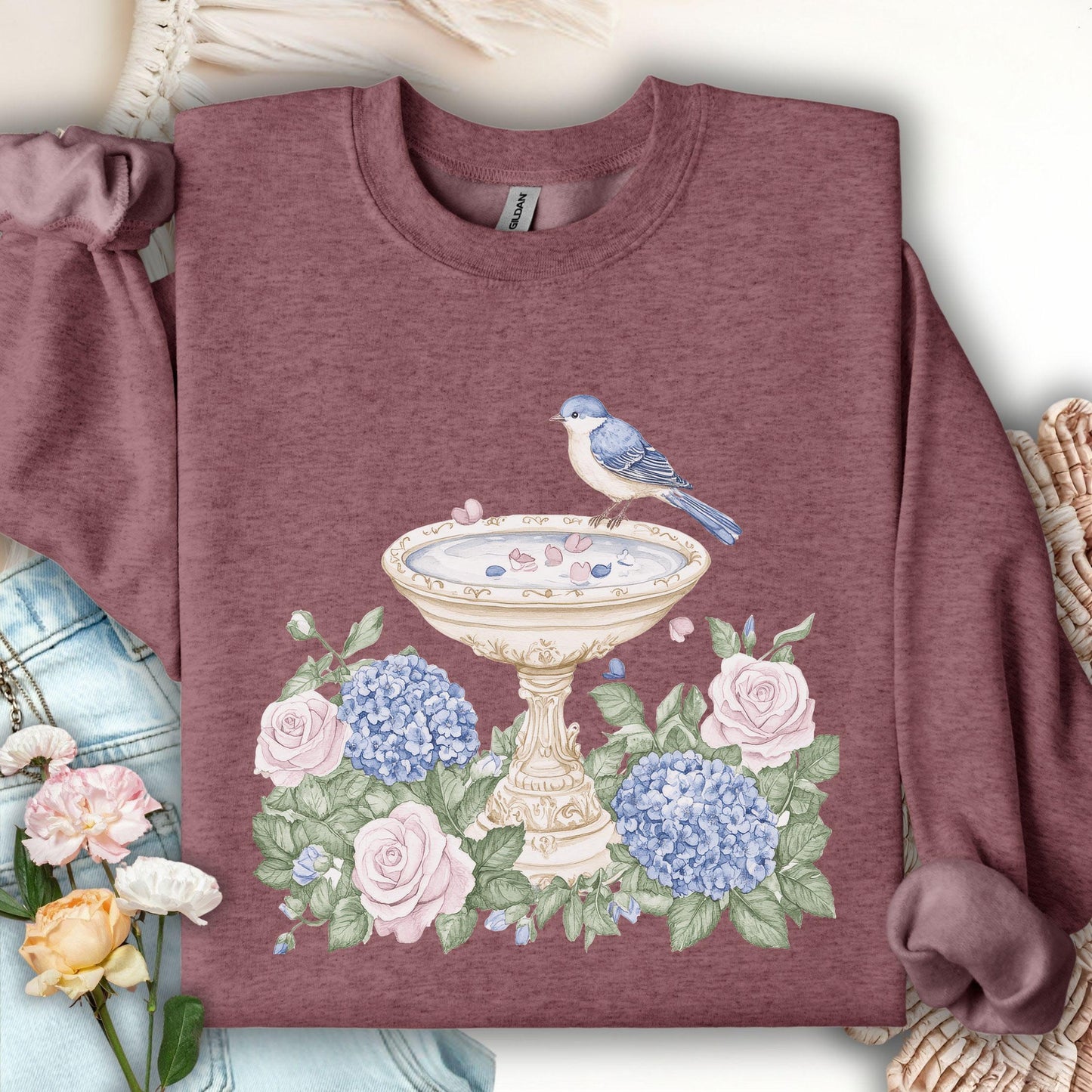 Heather Sport Dark Maroon sweatshirt with a watercolor bird bath, blue bird, pink roses, and blue hydrangeas.
