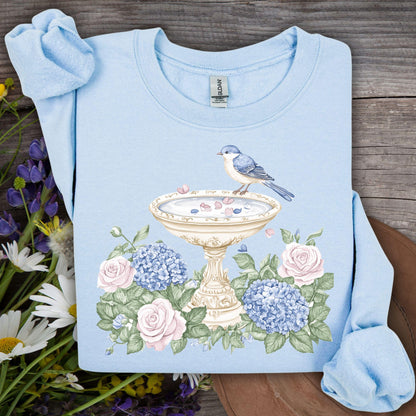 Light blue sweatshirt with a watercolor bird bath, blue bird, pink roses, and blue hydrangeas.