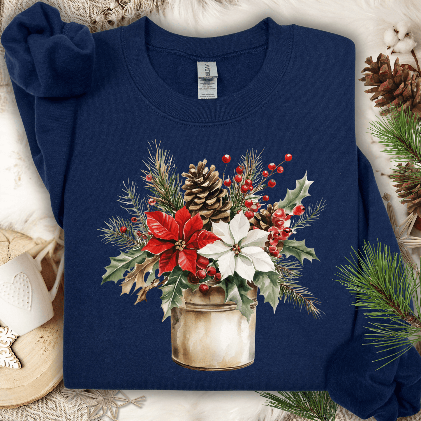 Navy Gildan sweatshirt with watercolor poinsettia bouquet in a rustic metal jar, surrounded by pinecones and holly.