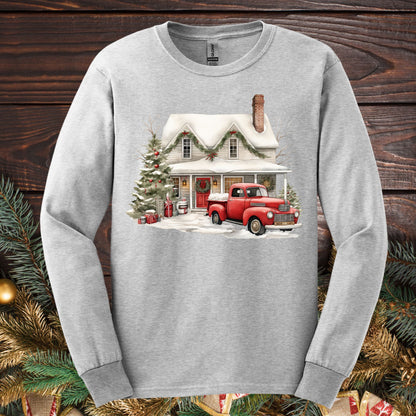 Ash gray Gildan long-sleeve tee with a watercolor farmhouse Christmas scene: red pickup, snow, evergreens.