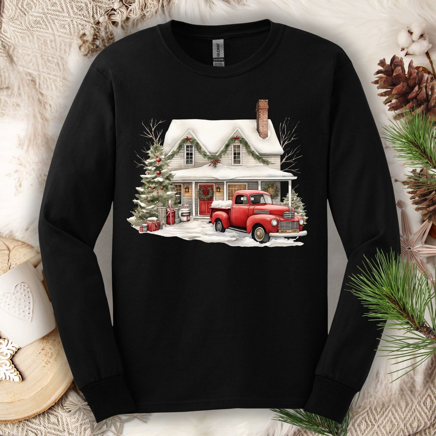 Black Gildan long sleeve tee with a watercolor farmhouse Christmas scene: red truck, snow, and evergreens.