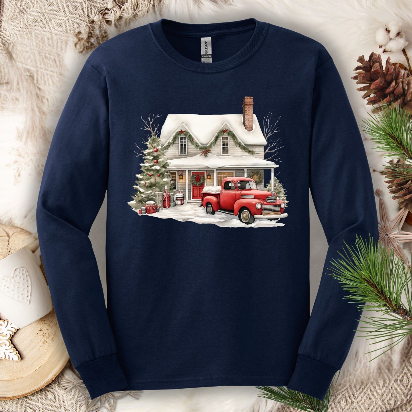 Navy long-sleeve tee with a watercolor farmhouse Christmas scene: red truck, snow, and evergreens.