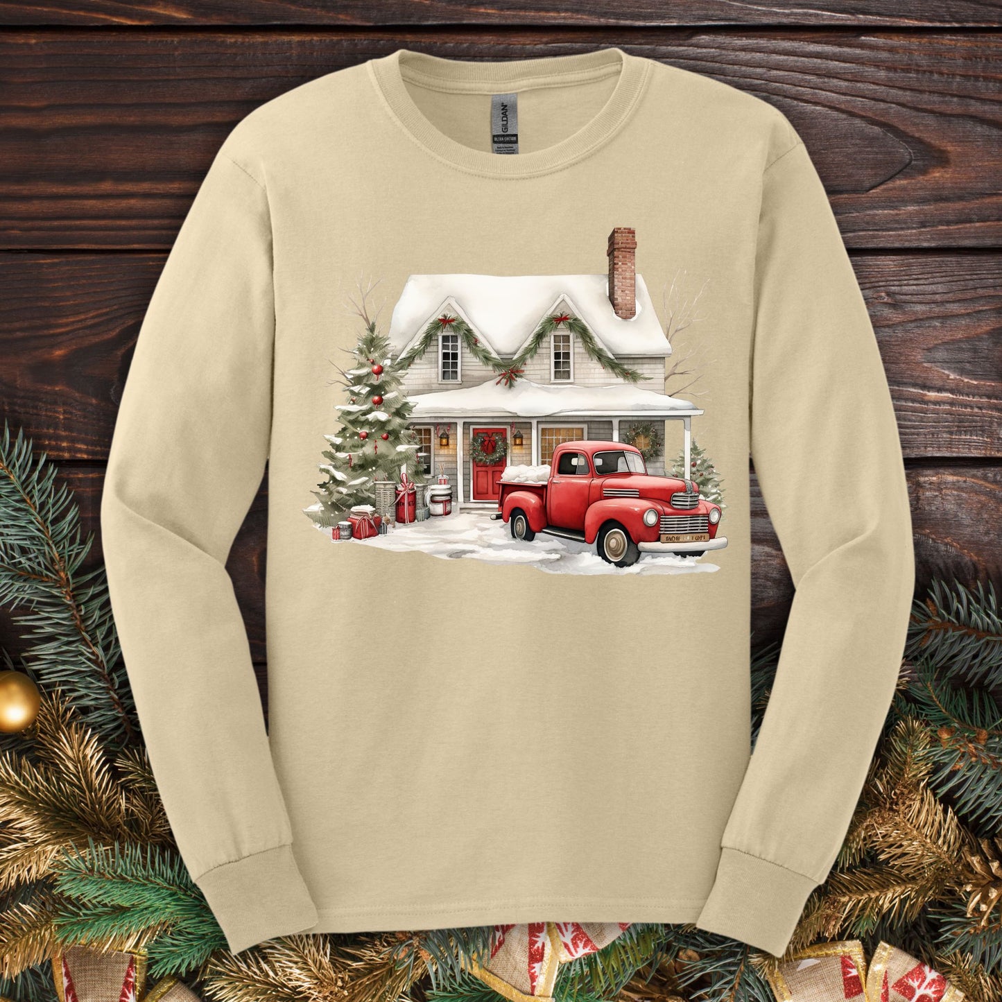 Sand long-sleeve tee with watercolor farmhouse Christmas scene: red pickup, snow, evergreens.