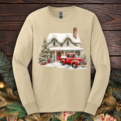 Sand long-sleeve tee with watercolor farmhouse Christmas scene: red pickup, snow, evergreens.