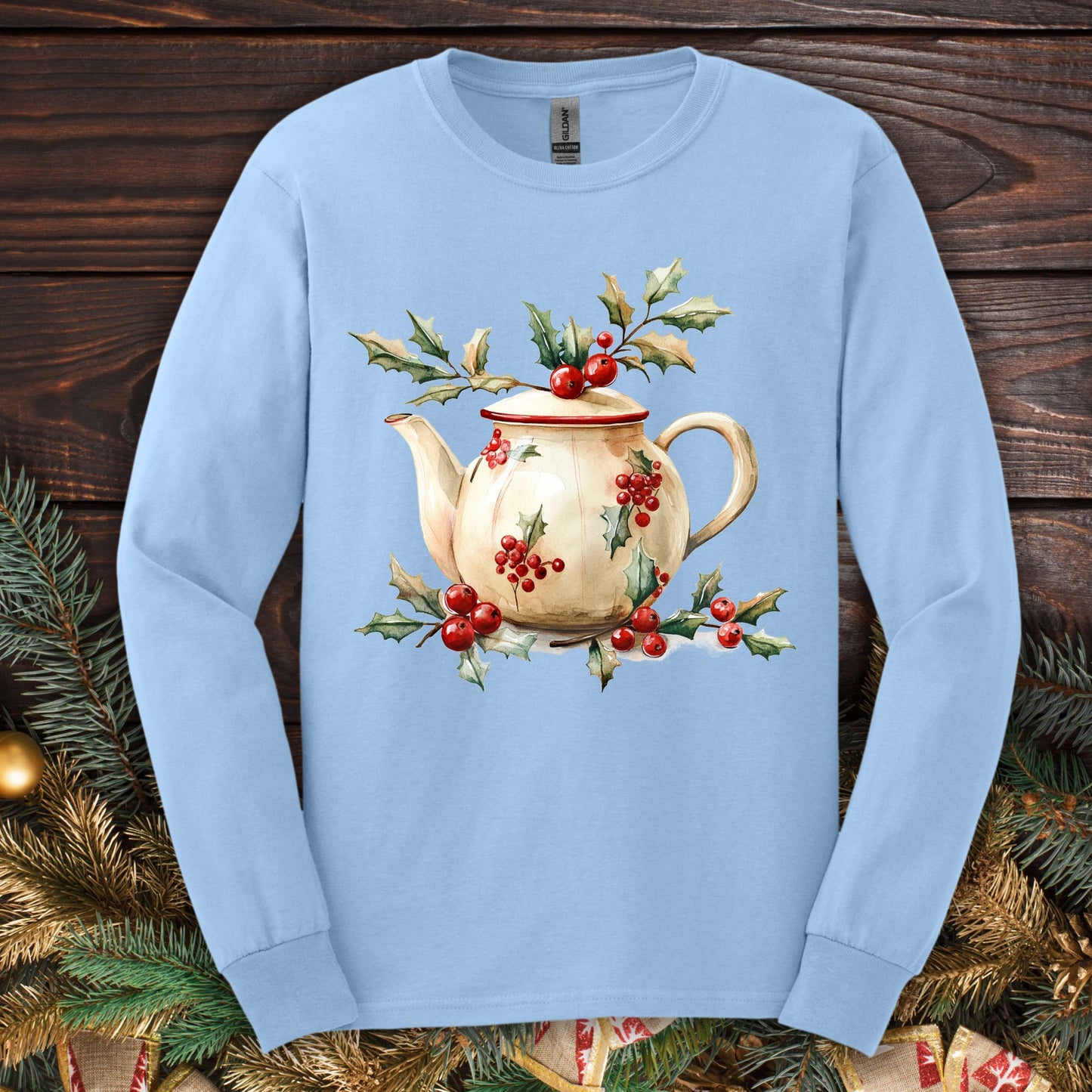 Light blue long sleeve tee with a watercolor farmhouse Christmas teapot, holly, and evergreens.