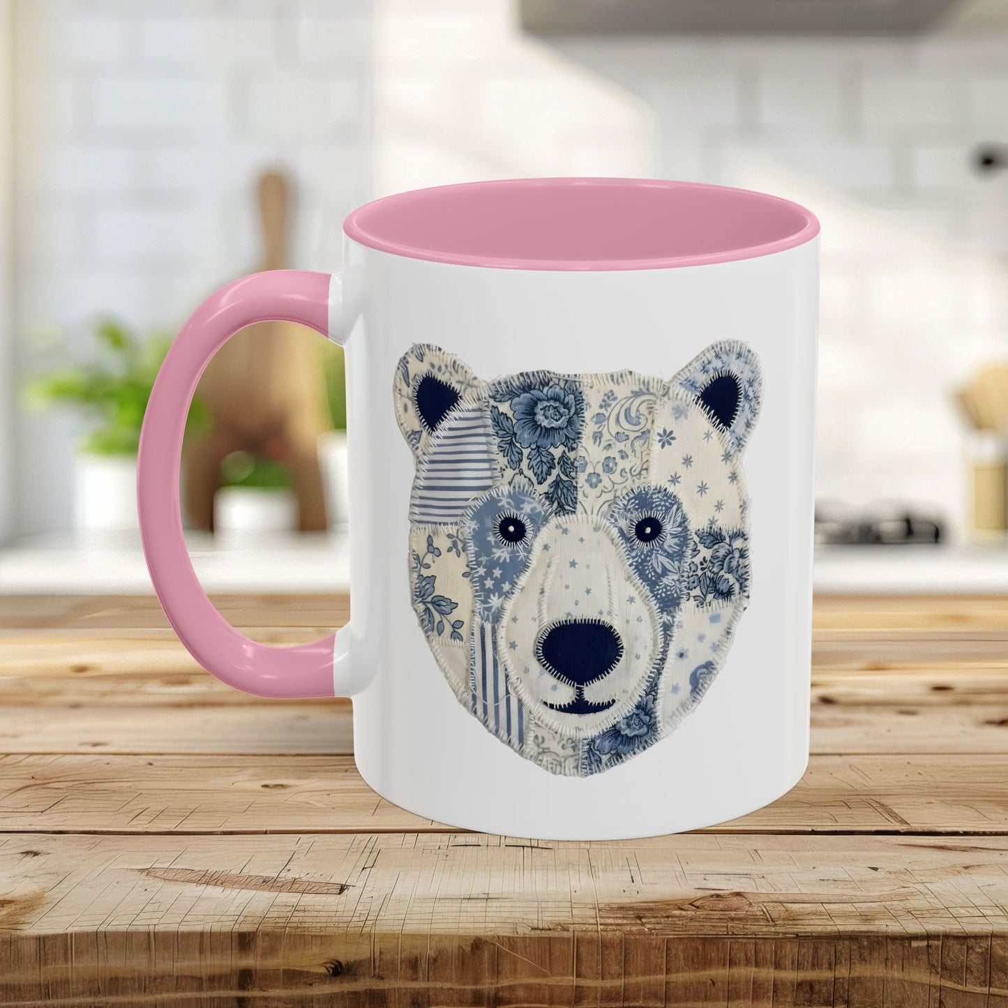 White ceramic mug with pink handle and interior, featuring a blue and white faux patchwork winter bear face.