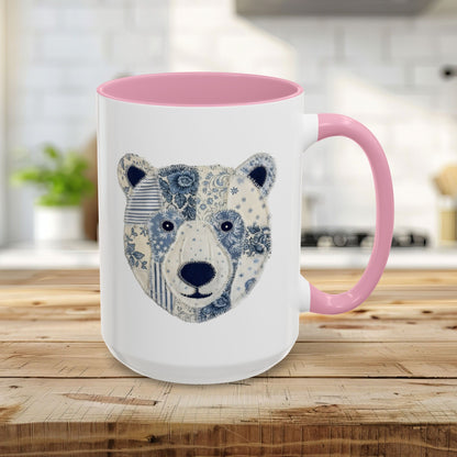 White ceramic mug with pink handle and rim, featuring a faux patchwork blue and white winter bear face.