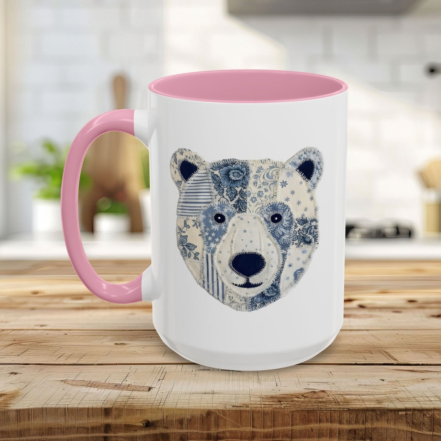 White ceramic mug with pink rim and handle, featuring a blue and white faux patchwork winter bear face.