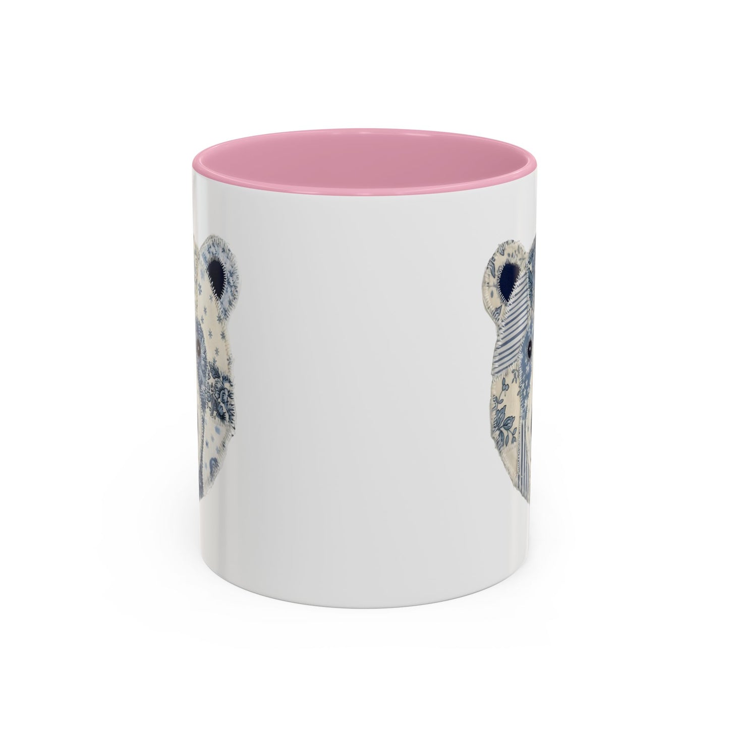 White ceramic mug with pink rim and handle, featuring a blue and white faux patchwork winter bear face.