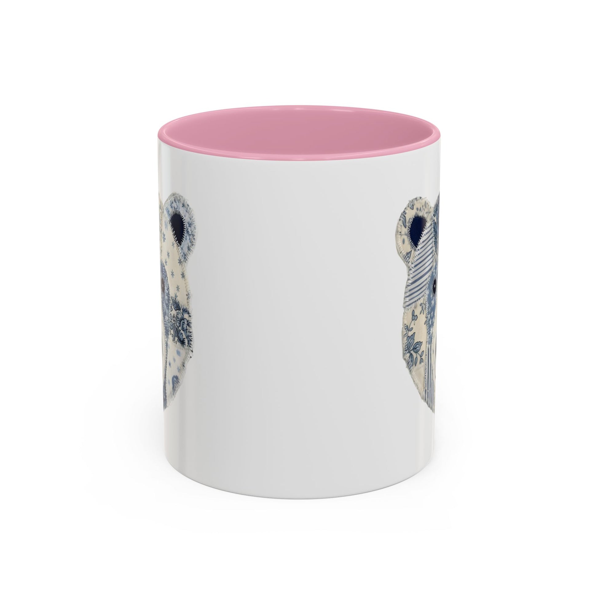 White ceramic mug with pink rim and handle, featuring a blue and white faux patchwork winter bear face.