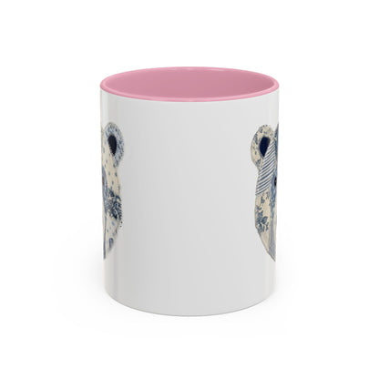 White ceramic mug with pink rim and handle, featuring a blue and white faux patchwork winter bear face.