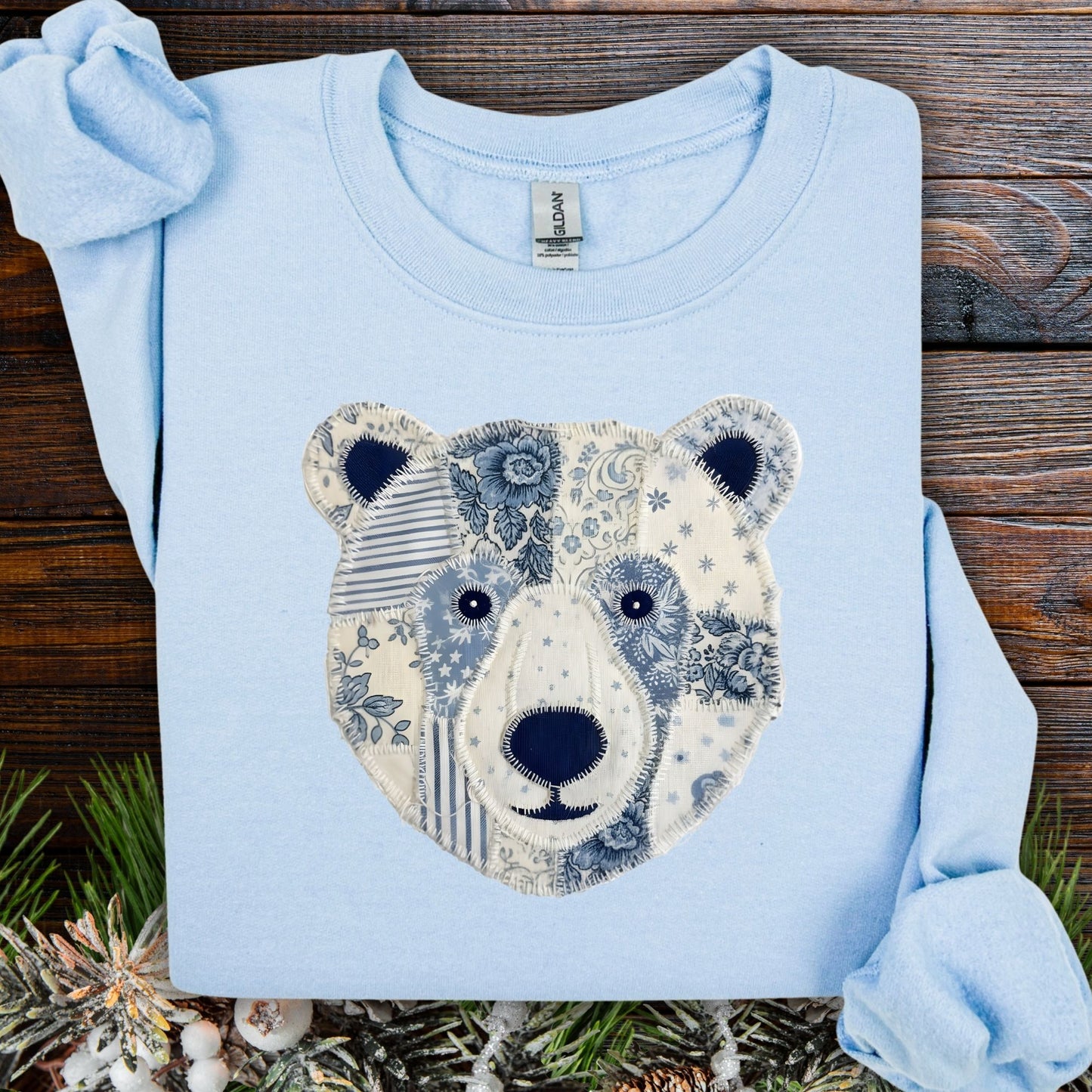 Light blue cotton-polyester sweatshirt with a faux patchwork country winter bear design in blue and white.