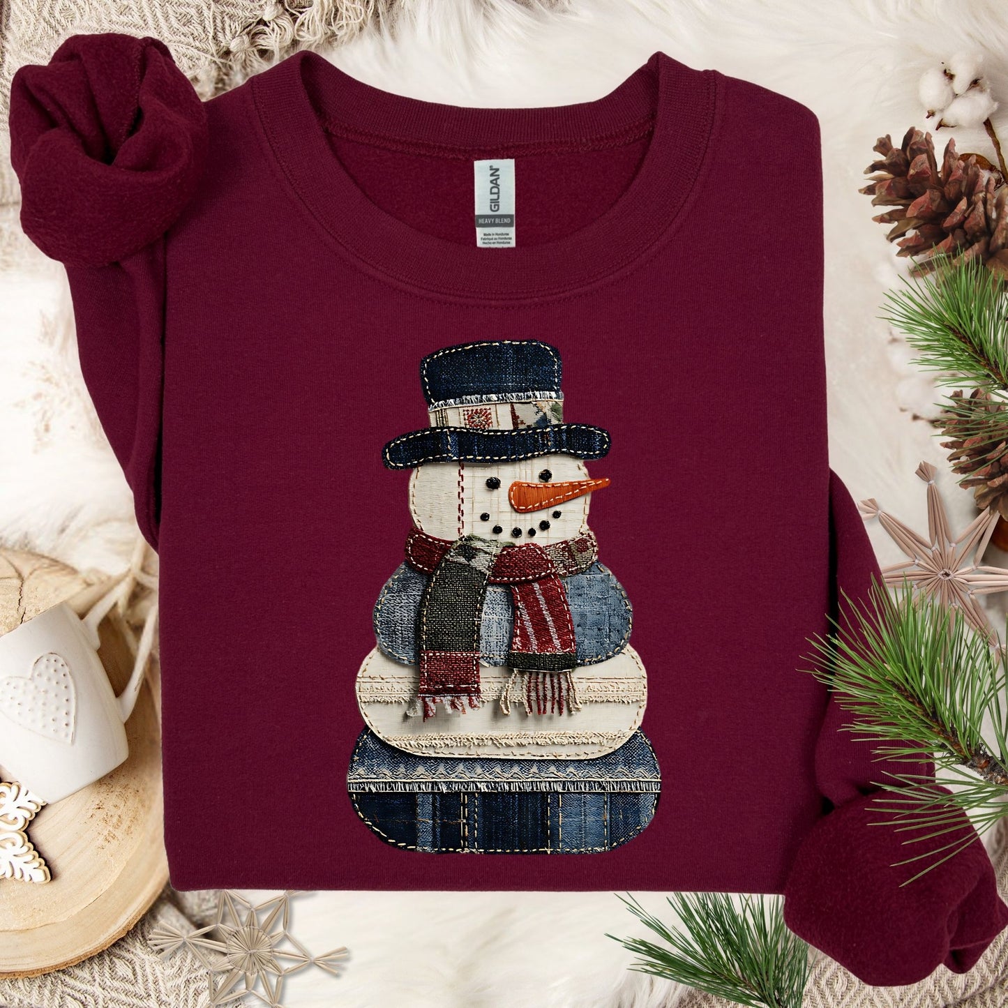 Maroon Gildan sweatshirt with a faux patchwork denim snowman design, surrounded by winter decor.